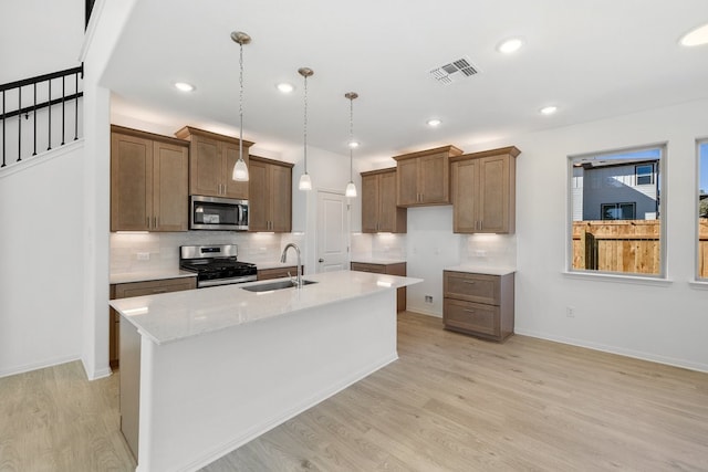 kitchen with pendant lighting, a kitchen island with sink, sink, and appliances with stainless steel finishes