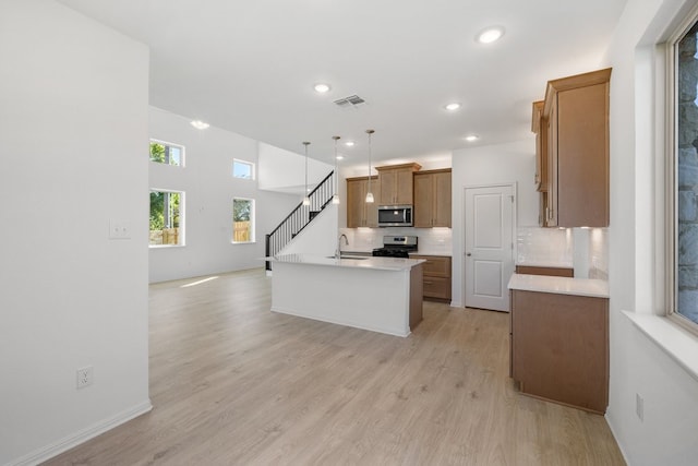 kitchen featuring decorative backsplash, stainless steel appliances, a kitchen island with sink, decorative light fixtures, and light hardwood / wood-style floors