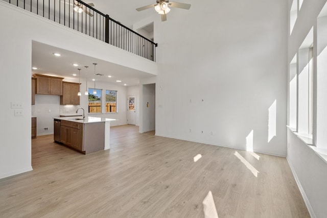 kitchen with a towering ceiling, light hardwood / wood-style flooring, hanging light fixtures, and an island with sink