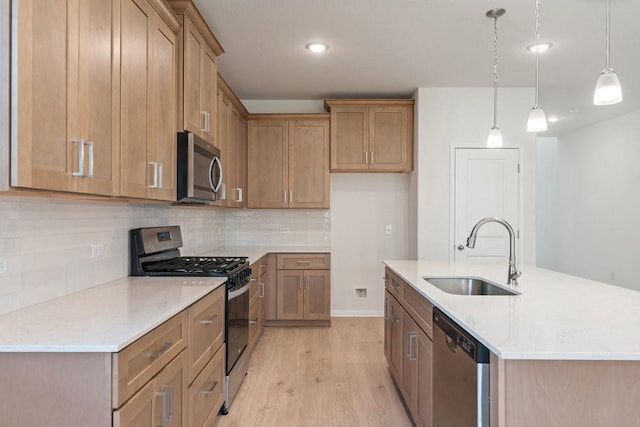 kitchen featuring sink, stainless steel appliances, pendant lighting, light hardwood / wood-style floors, and a center island with sink