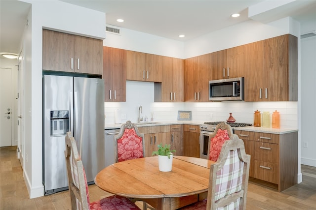 kitchen with light hardwood / wood-style flooring, backsplash, appliances with stainless steel finishes, and sink