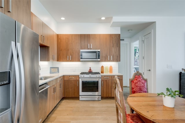 kitchen with light hardwood / wood-style floors, appliances with stainless steel finishes, tasteful backsplash, and sink