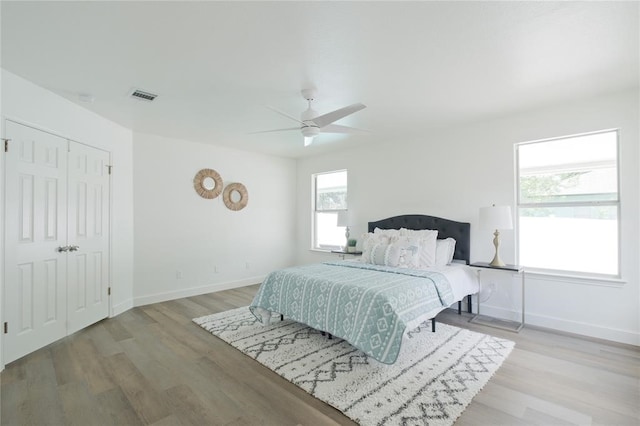 bedroom with light hardwood / wood-style flooring, a closet, multiple windows, and ceiling fan