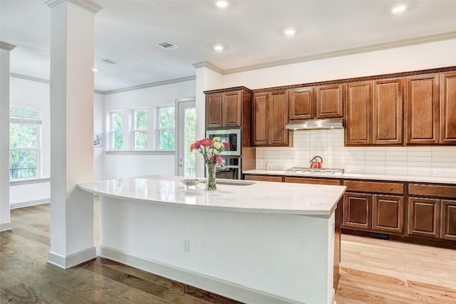 kitchen with stainless steel appliances, crown molding, a center island with sink, and light hardwood / wood-style floors