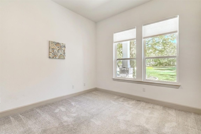 spare room with a healthy amount of sunlight, baseboards, and light colored carpet