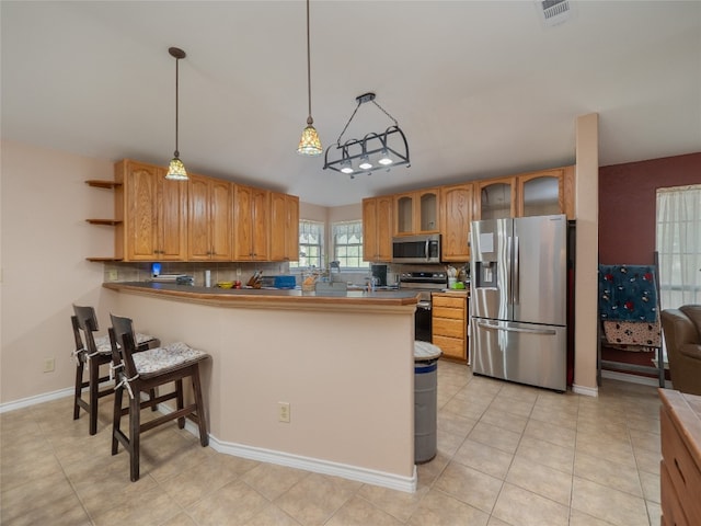 kitchen featuring tasteful backsplash, a breakfast bar area, decorative light fixtures, kitchen peninsula, and appliances with stainless steel finishes