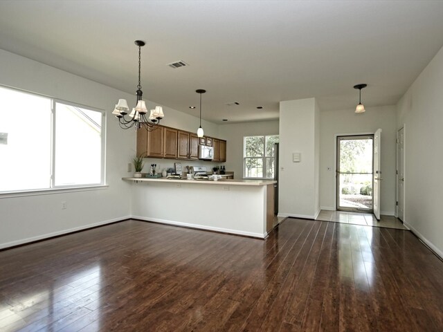 kitchen featuring kitchen peninsula, dark hardwood / wood-style flooring, stainless steel stove, pendant lighting, and a chandelier