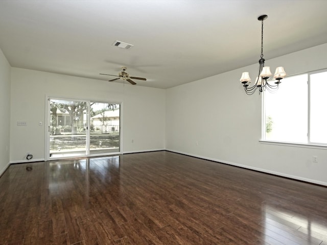 unfurnished room featuring a healthy amount of sunlight, ceiling fan with notable chandelier, and dark hardwood / wood-style flooring