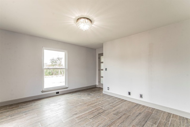 unfurnished room featuring a notable chandelier and light wood-type flooring