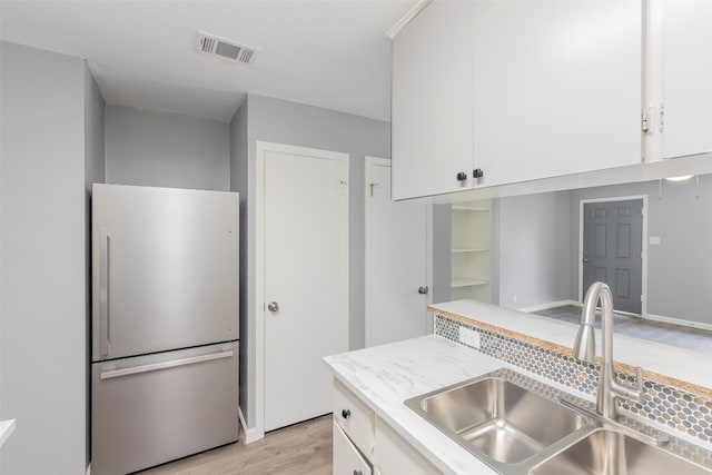 kitchen with white cabinets, stainless steel refrigerator, light hardwood / wood-style flooring, and sink