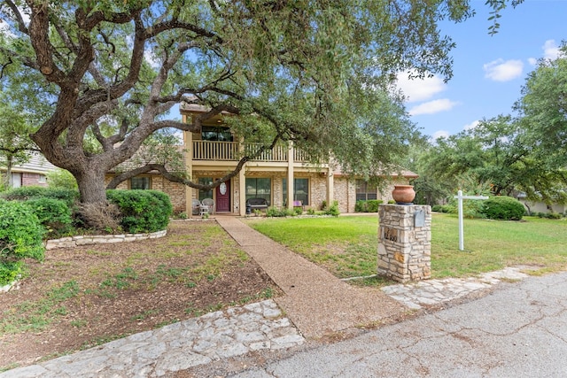 view of property hidden behind natural elements featuring a balcony and a front lawn