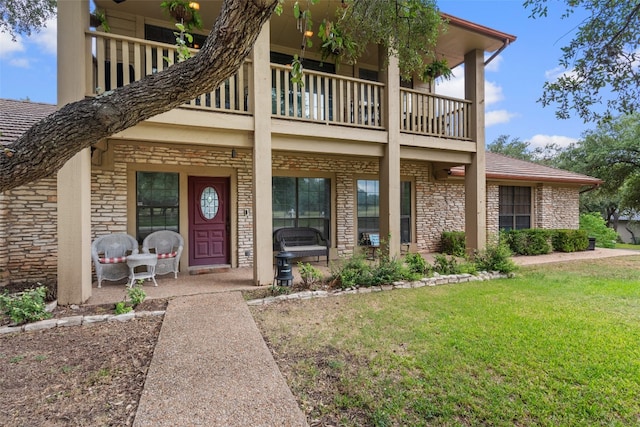 view of exterior entry with a lawn and a balcony