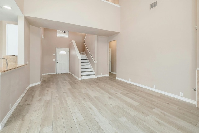 unfurnished living room with light wood-type flooring and a high ceiling