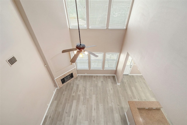 unfurnished living room featuring ceiling fan, light wood-type flooring, and a towering ceiling