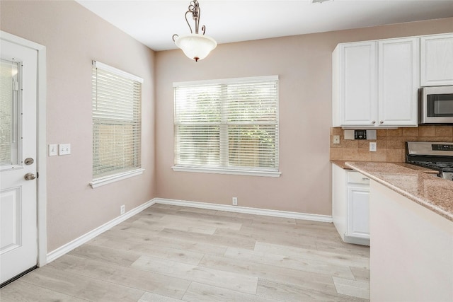 kitchen with white cabinets, decorative light fixtures, backsplash, light hardwood / wood-style flooring, and stainless steel appliances