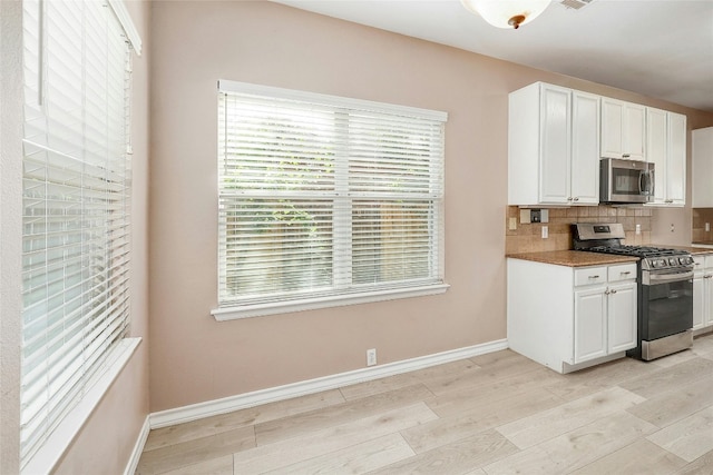 kitchen with appliances with stainless steel finishes, decorative backsplash, light hardwood / wood-style floors, and white cabinets