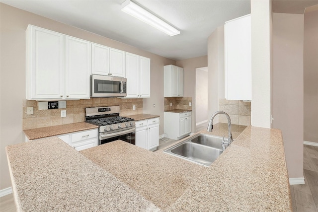 kitchen featuring white cabinets, sink, kitchen peninsula, tasteful backsplash, and stainless steel appliances