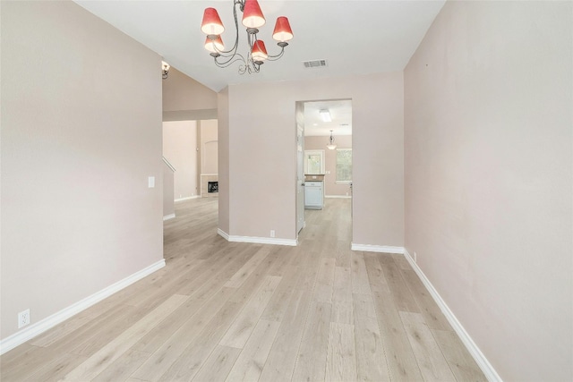 spare room with an inviting chandelier and light hardwood / wood-style floors