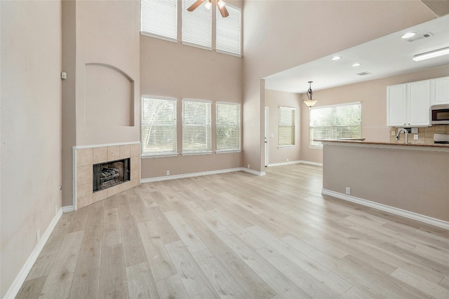 unfurnished living room featuring a high ceiling, a tiled fireplace, ceiling fan, and light hardwood / wood-style flooring