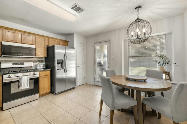 kitchen with an inviting chandelier, appliances with stainless steel finishes, tasteful backsplash, decorative light fixtures, and light tile patterned flooring