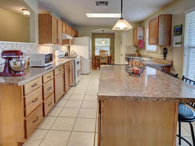 kitchen featuring pendant lighting, white appliances, a kitchen bar, and a healthy amount of sunlight