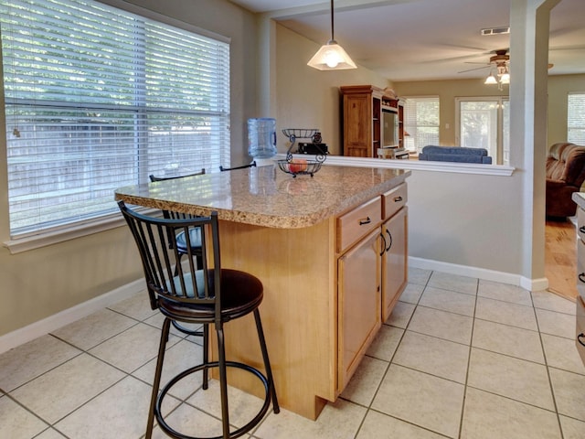 kitchen with ceiling fan, light tile patterned floors, decorative light fixtures, a kitchen breakfast bar, and a center island