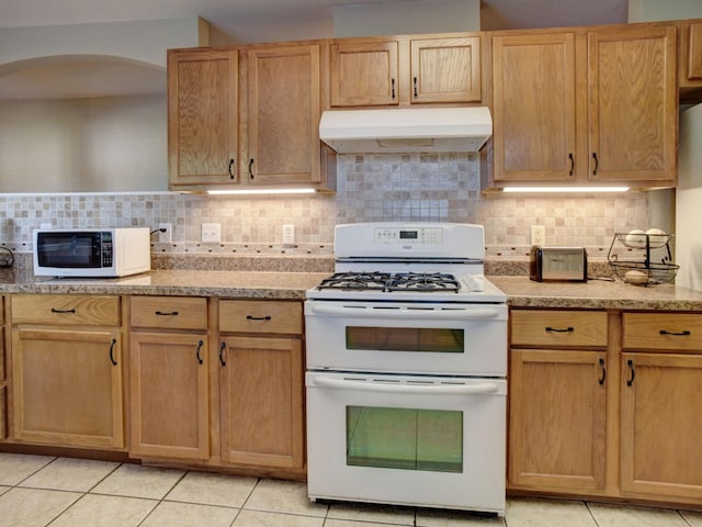 kitchen with light stone counters, light tile patterned flooring, backsplash, and white appliances