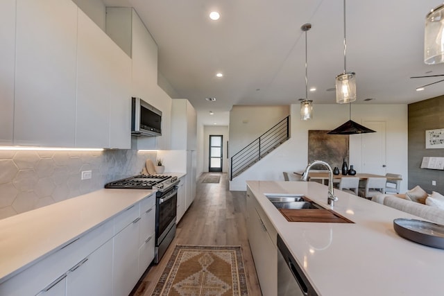 kitchen featuring white cabinetry, sink, stainless steel appliances, tasteful backsplash, and decorative light fixtures