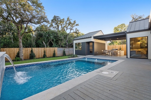 view of pool featuring a wooden deck, pool water feature, exterior bar, and an outdoor structure