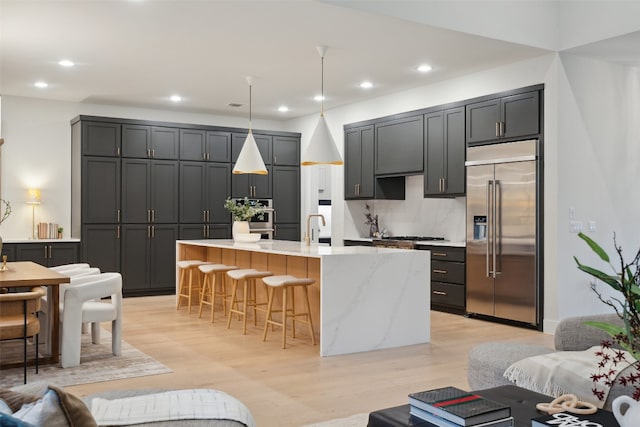 kitchen with a kitchen breakfast bar, light hardwood / wood-style flooring, decorative light fixtures, a center island with sink, and appliances with stainless steel finishes