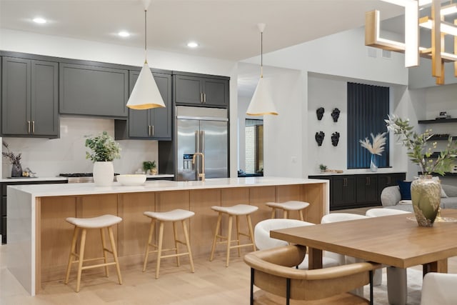 kitchen with a kitchen breakfast bar, a kitchen island with sink, built in fridge, and gray cabinetry