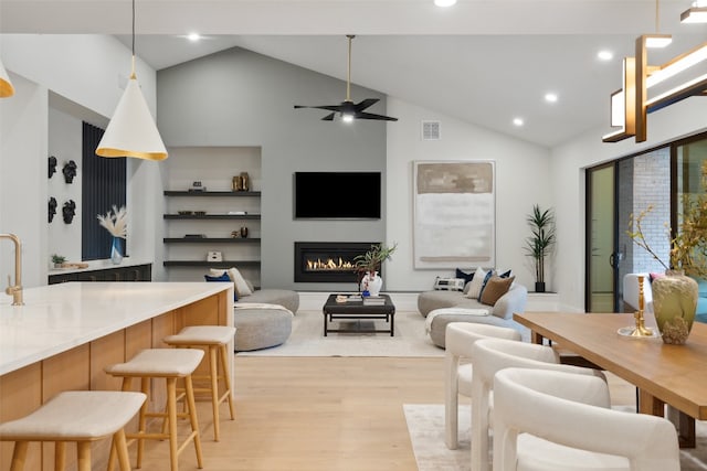 living room with ceiling fan, high vaulted ceiling, and light hardwood / wood-style floors