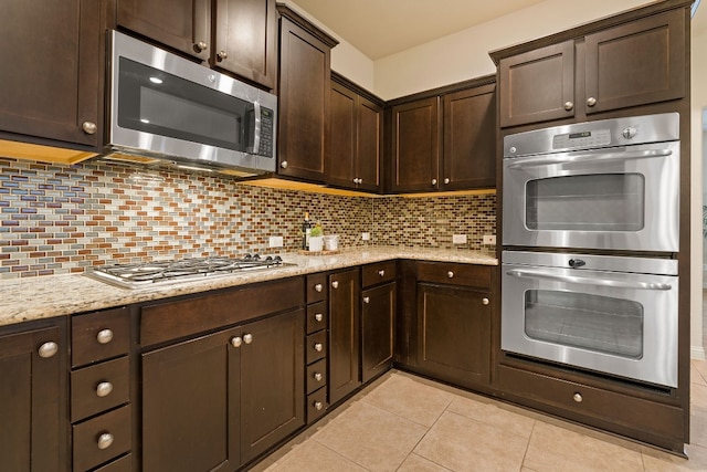 kitchen featuring light tile patterned flooring, dark brown cabinetry, light stone counters, decorative backsplash, and appliances with stainless steel finishes