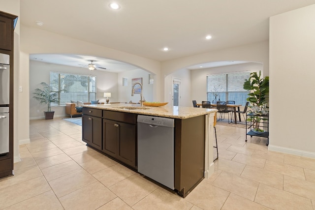 kitchen with light tile patterned flooring, sink, stainless steel dishwasher, a kitchen island with sink, and light stone countertops