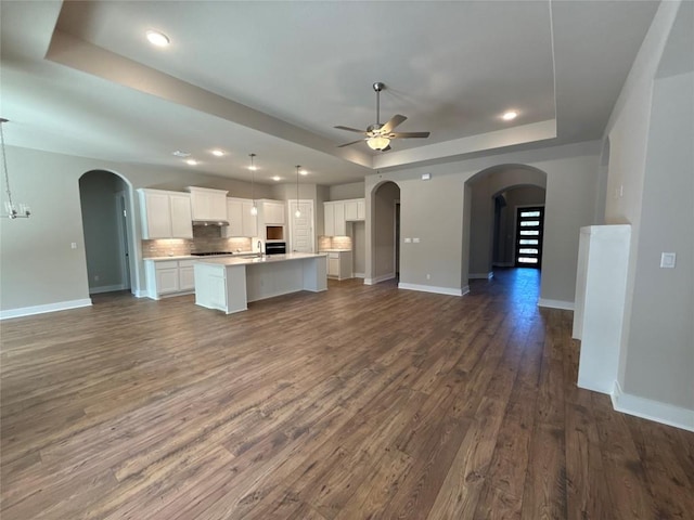 unfurnished living room with ceiling fan with notable chandelier, dark hardwood / wood-style floors, a tray ceiling, and sink