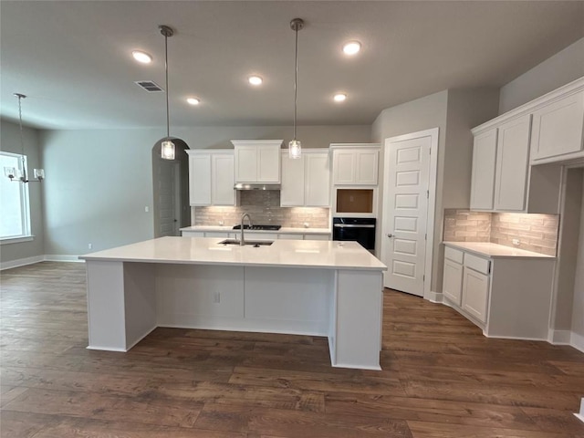 kitchen with pendant lighting, stainless steel oven, a kitchen island with sink, dark hardwood / wood-style floors, and white cabinetry