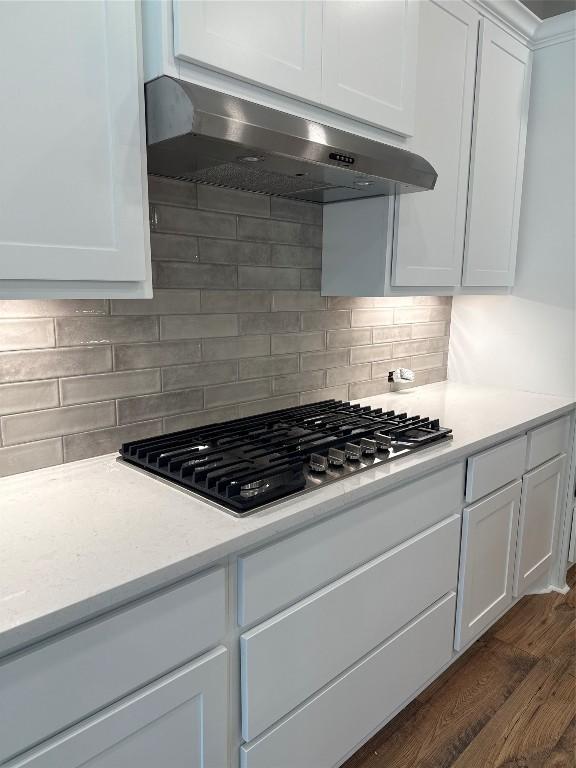 kitchen with dark wood-type flooring, stainless steel gas cooktop, tasteful backsplash, range hood, and white cabinets