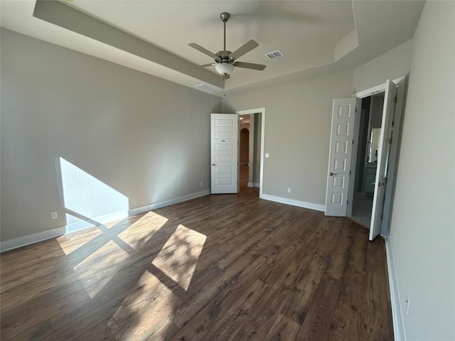 unfurnished bedroom featuring a tray ceiling, ceiling fan, and dark wood-type flooring