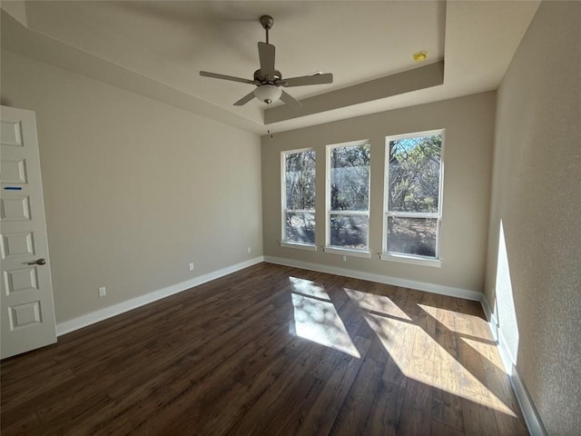 empty room featuring dark hardwood / wood-style floors, ceiling fan, and a tray ceiling