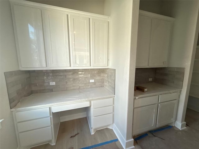 kitchen with backsplash, white cabinetry, light hardwood / wood-style flooring, and built in desk