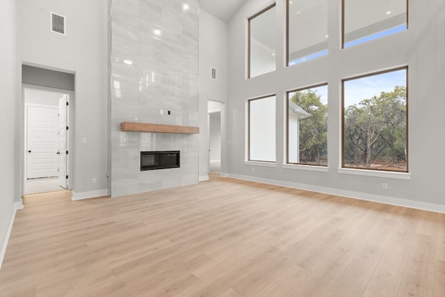 unfurnished living room featuring a tile fireplace, a towering ceiling, and light hardwood / wood-style flooring