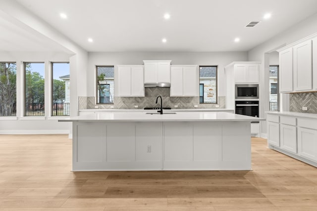 kitchen featuring stainless steel microwave, sink, and an island with sink