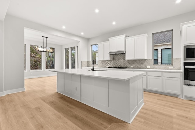 kitchen with a kitchen island with sink, oven, and white cabinets