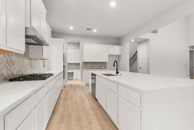 kitchen featuring a spacious island, sink, appliances with stainless steel finishes, light stone countertops, and white cabinets