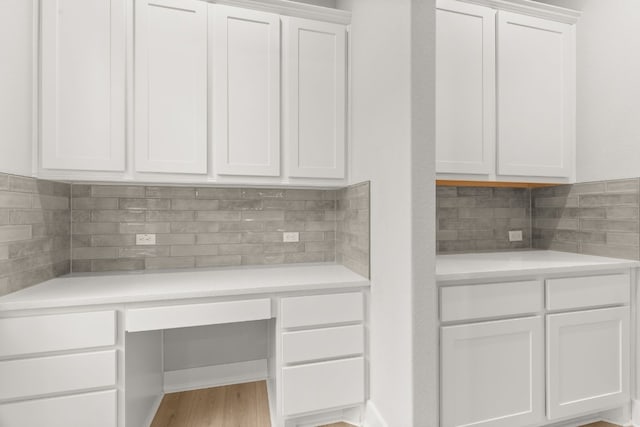 kitchen with built in desk, light wood-type flooring, decorative backsplash, and white cabinets