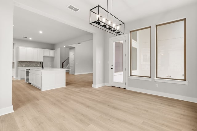 kitchen with a kitchen island with sink, white cabinets, pendant lighting, light hardwood / wood-style floors, and backsplash