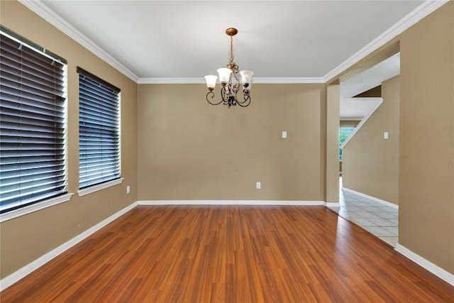 spare room featuring wood-type flooring, ornamental molding, and a chandelier