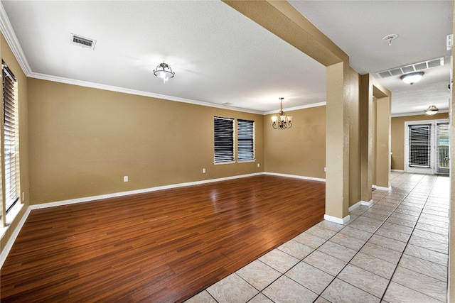 spare room featuring a textured ceiling, light wood-type flooring, crown molding, and a chandelier