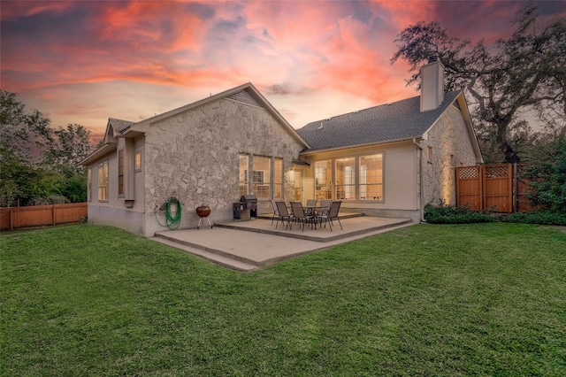 back house at dusk featuring a patio area and a lawn