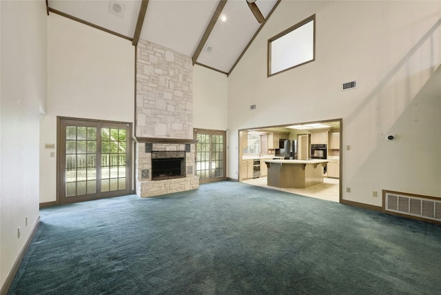 unfurnished living room with high vaulted ceiling, a stone fireplace, beamed ceiling, ceiling fan, and carpet